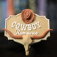 Etichetă 3D Cowboy Romance în stil western, cu formă de insignă, pălărie de cowboy maro și un craniu de taur cu coarne lungi.