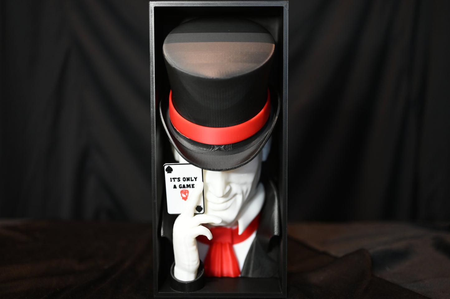 Booknook Legend - Inspirație Caraval Book nook cu figura misterioasă inspirată din Legend din Caraval, purtând joben negru cu bandă roșie și ținând o carte de joc ‘It’s Only a Game’, fotografiat pe fundal negru.