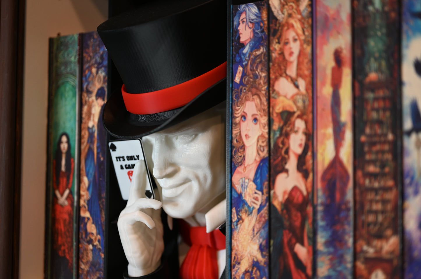 Book nook inspirat din Legend din Caraval, încadrat între cărți cu coperți ilustrate fantasy, cu joben negru și cartelă ‘It’s Only a Game’ în mână.