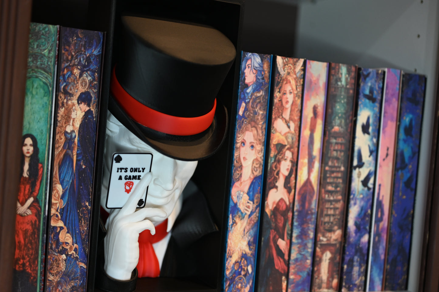 Book nook inspirat din Legend din Caraval, încadrat între cărți cu coperți ilustrate fantasy, cu joben negru și cartelă ‘It’s Only a Game’ în mână.