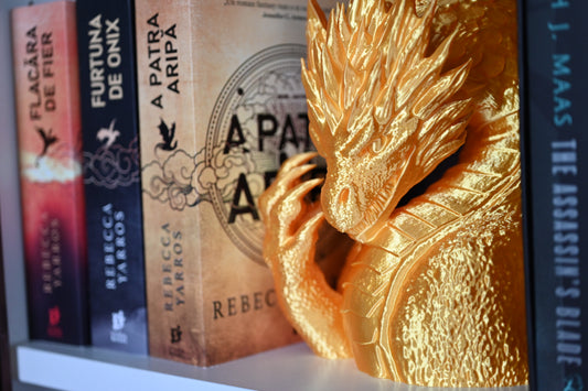 Statuetă decorativă pentru bibliotecă auriu impunator, stand intre cartile Rebeccai Yarros, pe un raft in biblioteca