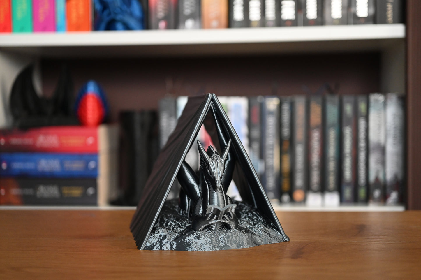 suport de carte cu forma triunghiulara si sculptura de dragon in fata unui raft de carti