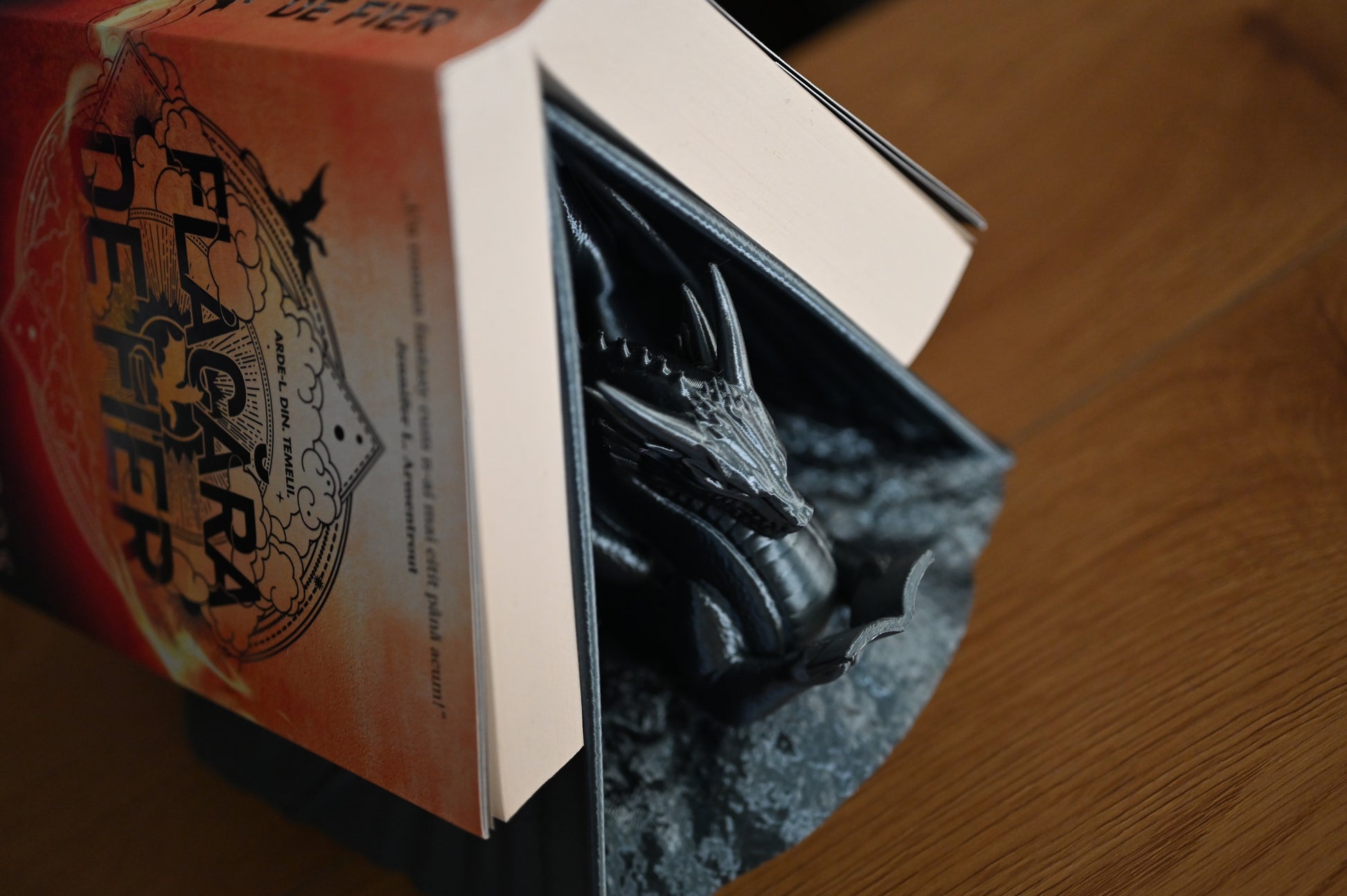 Suport decorativ pentru bibliotecă cu forma de dragon care sustine o carte scrisa de Rebecca Yarros