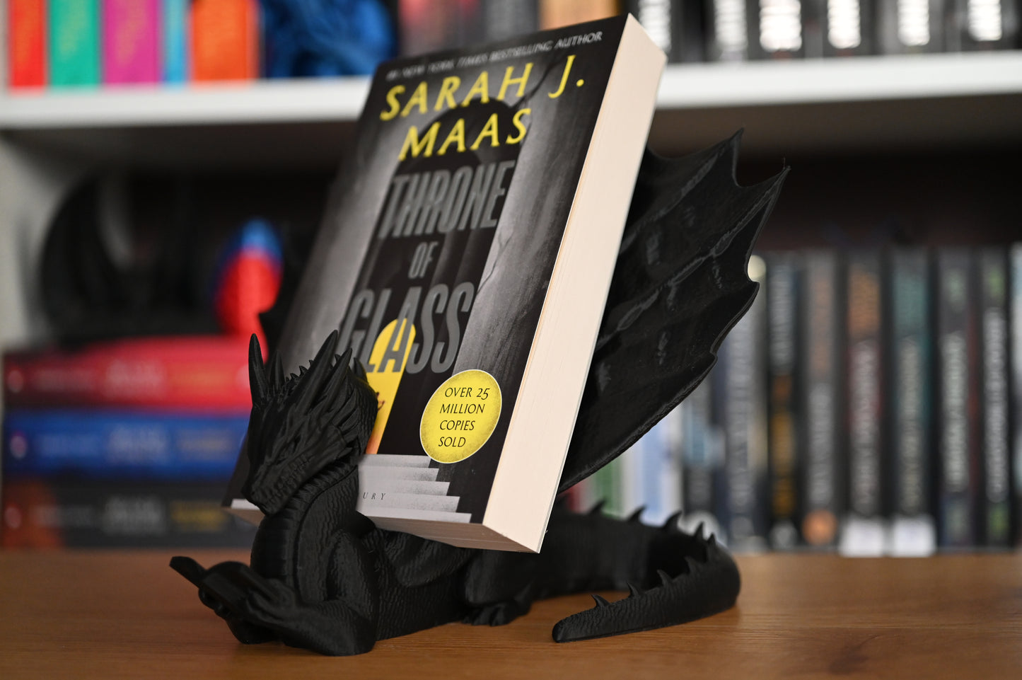 dragon negru in al carui suport de carte sta un volum scris de Sarah J. Maas