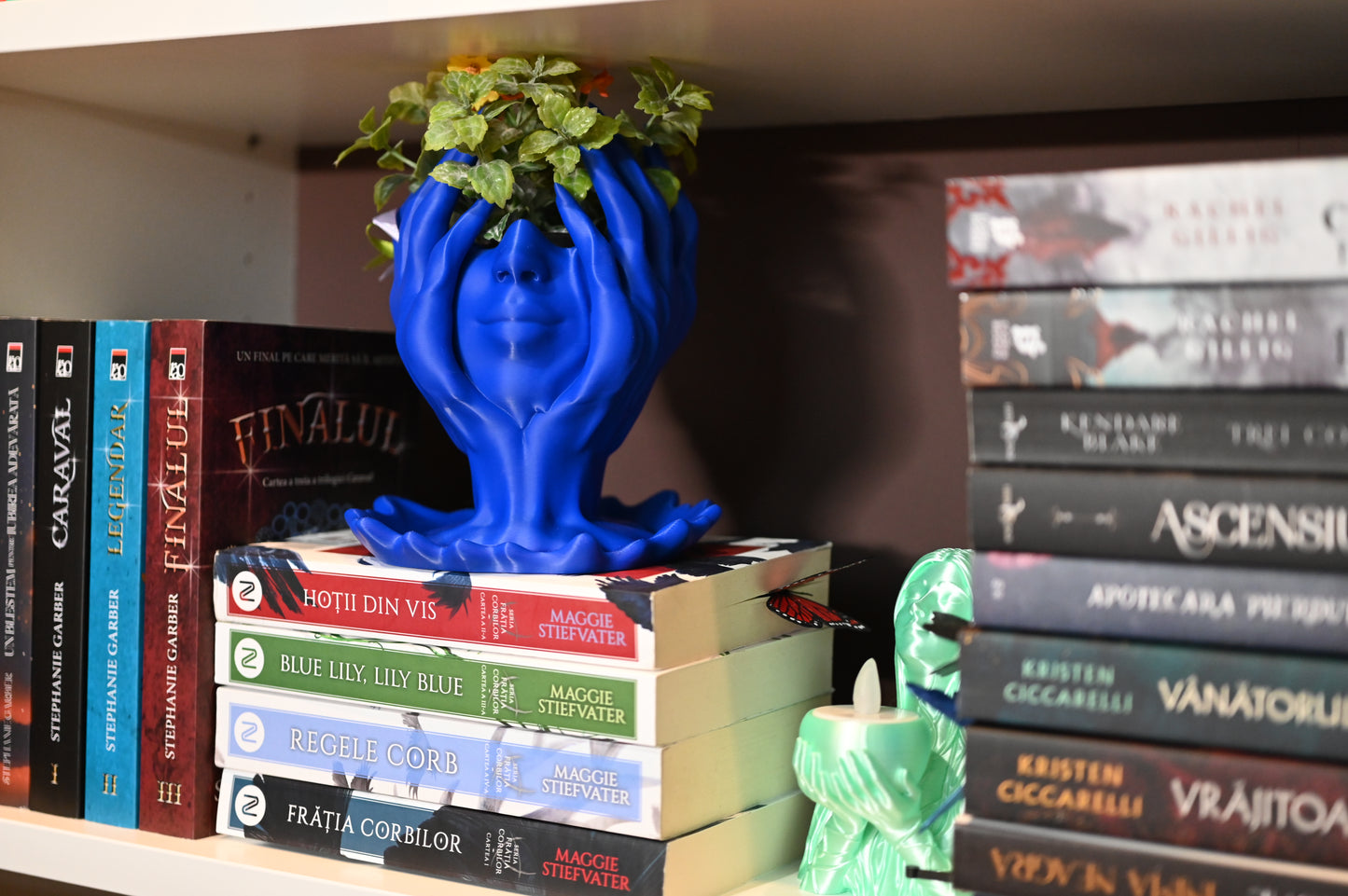 ghiveci decorativ cu fata unei femei care se sprijina in palme asezat intre carti