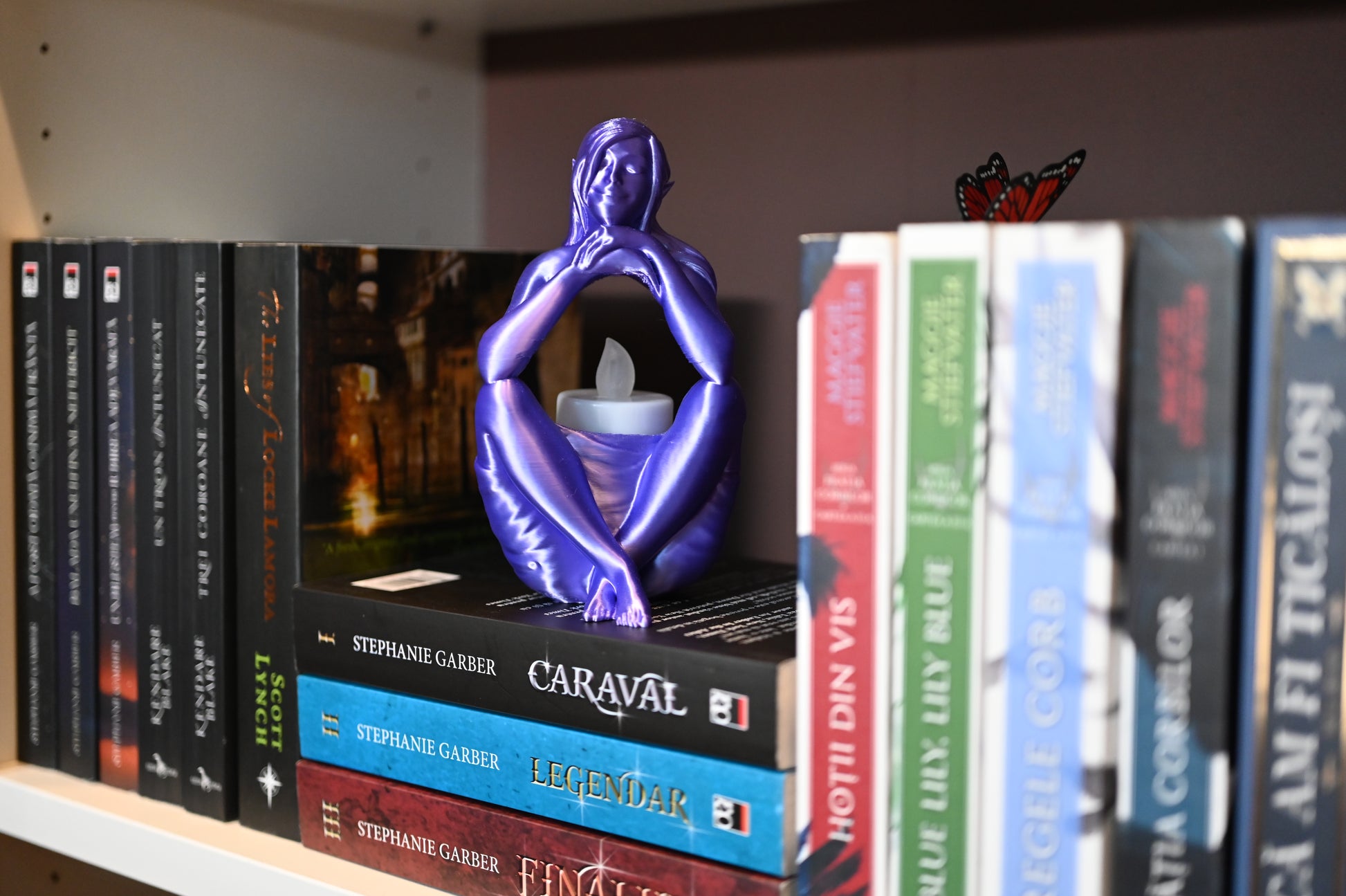Statuetă "Visul Elfului" mov stand pe cartile raftului unei biblioteci
