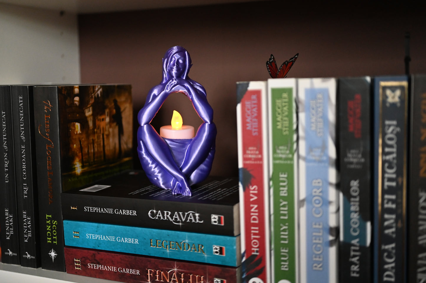 Statuetă "Visul Elfului" mov folosita ca suport decorativ de lumanare led, asezata pe un raft de biblioteca
