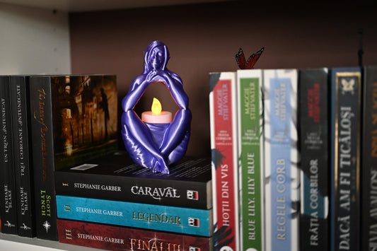 Statuetă "Visul Elfului" mov folosita ca suport decorativ de lumanare led, asezata pe un raft de biblioteca