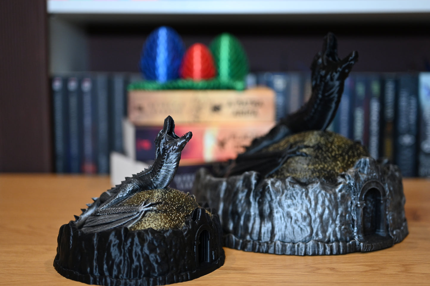 doua Figurine decorative cu dragoni, unul negru, celalalt argintiu, pe un munte auriu, lângă ouă de dragon colorate, pe fundal cu cartile scrise de Rebecca Yarros