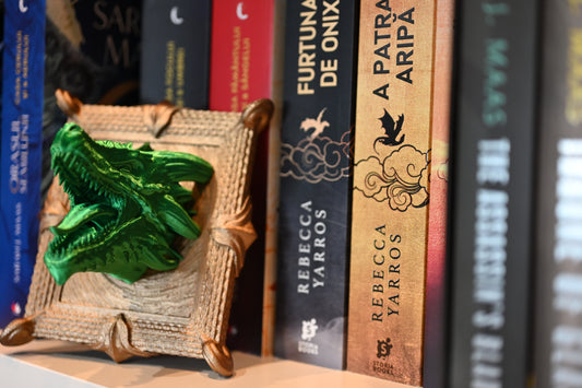 rama aurie din care iese in relief un cap de dragon 3D furios si verde, asezata langa cartile din seria Empyrean